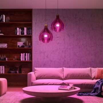 Philips Hue smart bulbs fitted to glass pendant lights fill a living room with pink tones of smart light.
