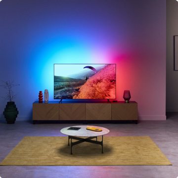TV ekranındaki renklerle senkronize olan TV Arka Aydınlatmasının etkileyici ışığıyla aydınlanan bir oturma odası.