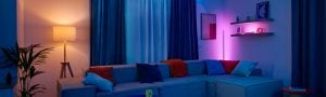 Ein Wohnzimmer mit einem Sofa, welches dezent beleuchtet wird durch eine WiZ Pole in einem Lila-Farbton und einer Stehleuchte in warmweißem Licht.