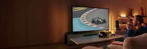 Een vader en zoon lachen terwijl ze op tv naar een razendsnelle autorace kijken, met WiZ Smart Lighting achter het scherm en op nabijgelegen planken.