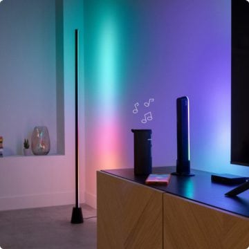 Un lampadar și o bară cu lumini în gradient amplasate lângă o bandă LED sincronizată cu televizorul luminează întreaga cameră de zi.