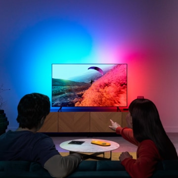 Ekranla senkronize renklere sahip LED ışıklı televizyonun keyfini çıkaran bir çift.